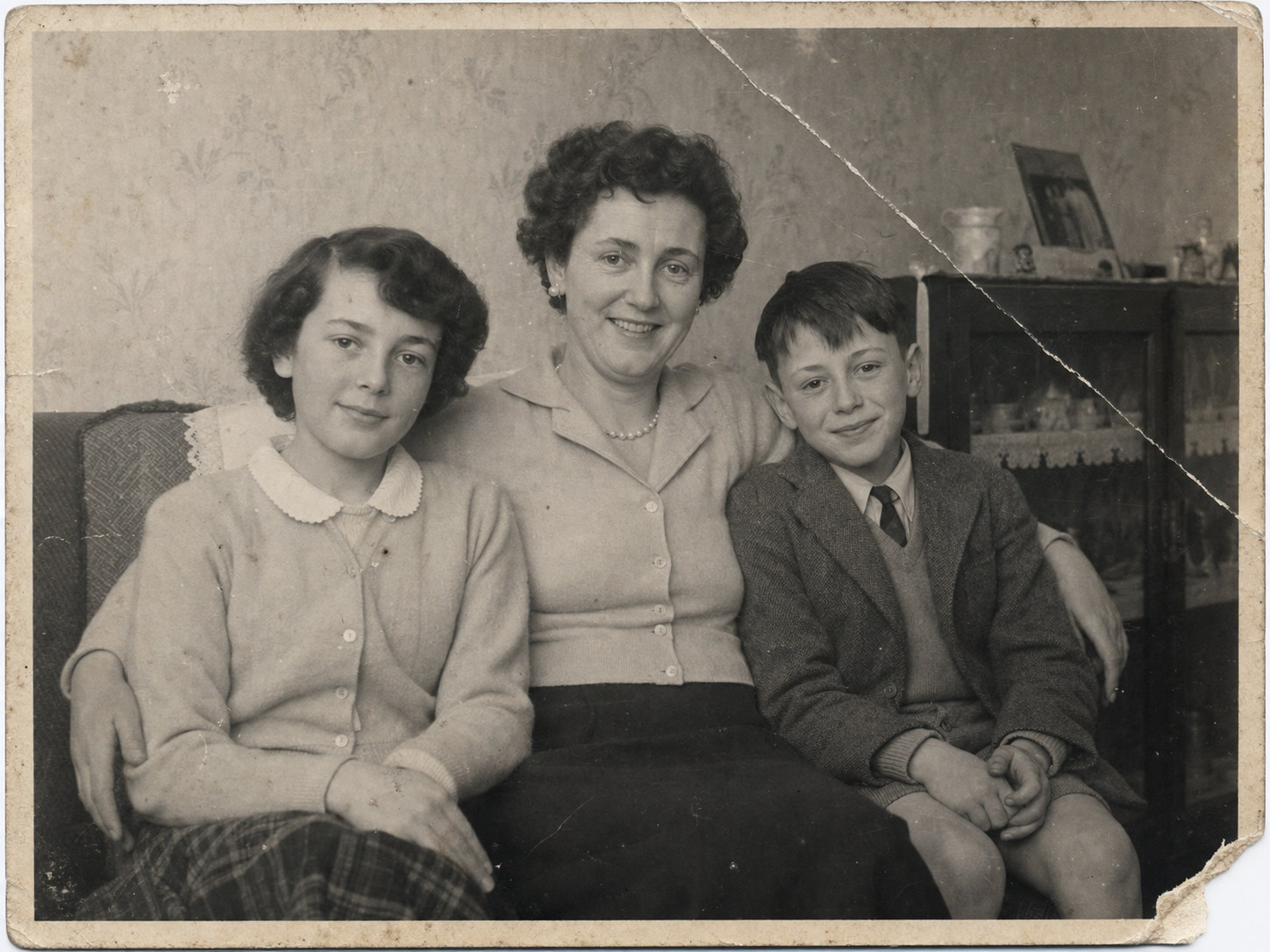 Generated black-and-white family photograph before restoration, showing a diagonal fold, fading, scratches and a torn corner.