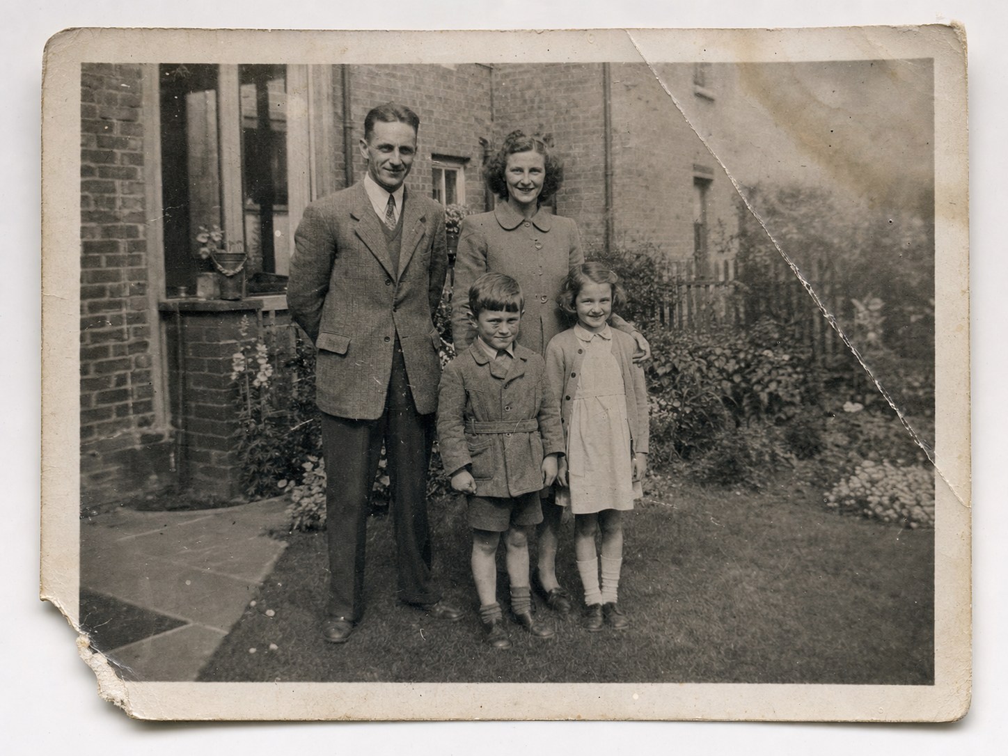 Generated black-and-white family photograph before restoration, showing a large crease, torn corner, fading and surface damage.